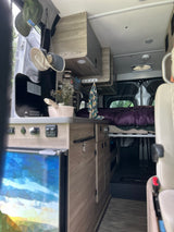 RV rental interior featuring a compact kitchen, bed, and smart storage solutions for cozy travels.