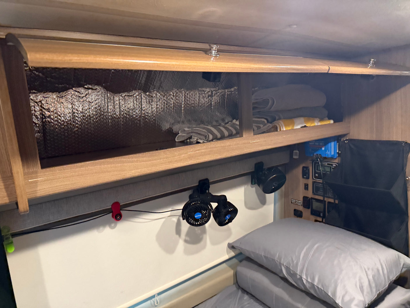 RV rental interior featuring overhead storage, clip-on fans, and control panel above a cozy bed, optimizing space.