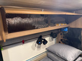 RV rental interior featuring overhead storage, clip-on fans, and control panel above a cozy bed, optimizing space.