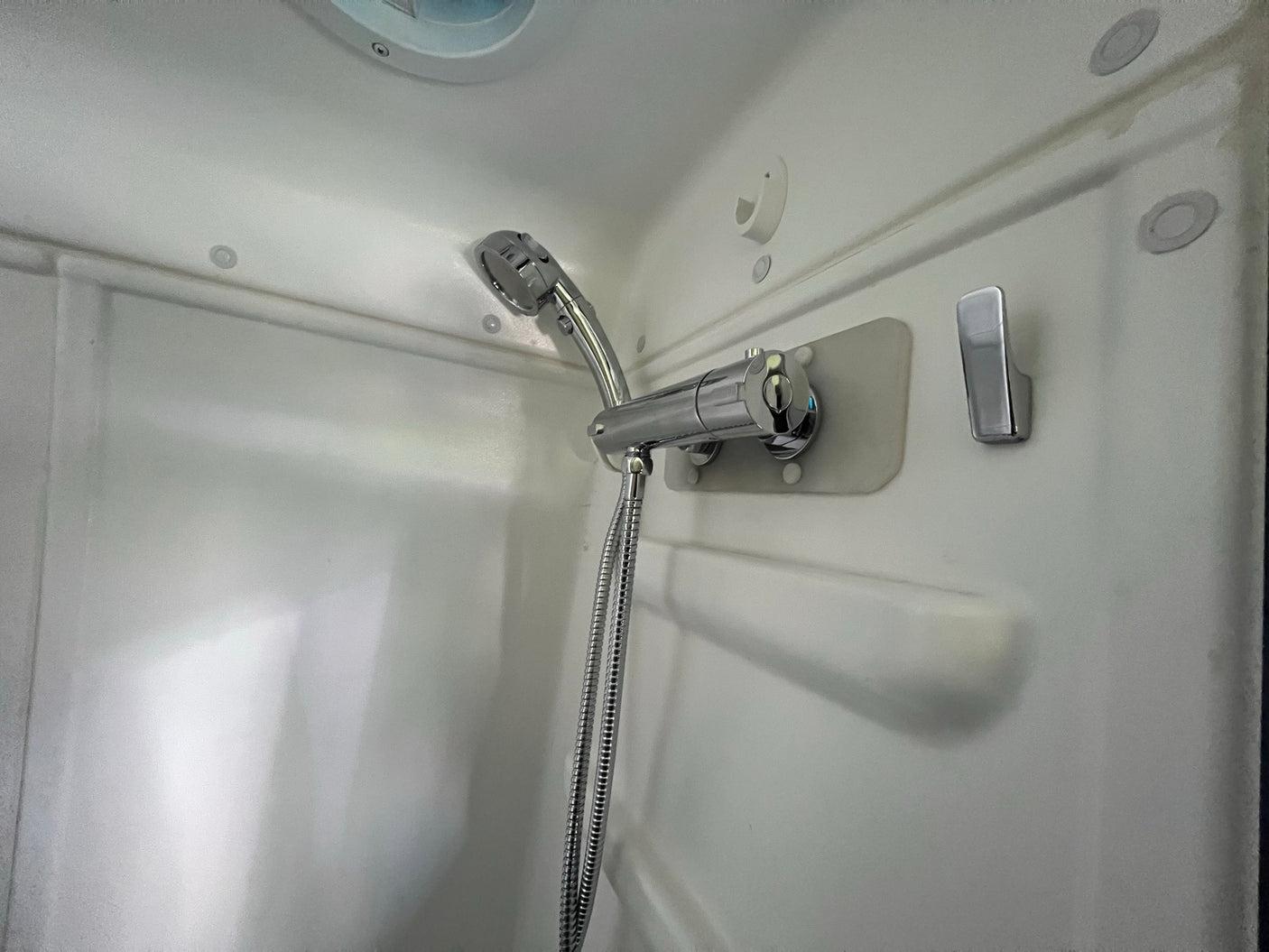 White RV rental shower with chrome handheld showerhead, hose, and faucet. Compact and functional.