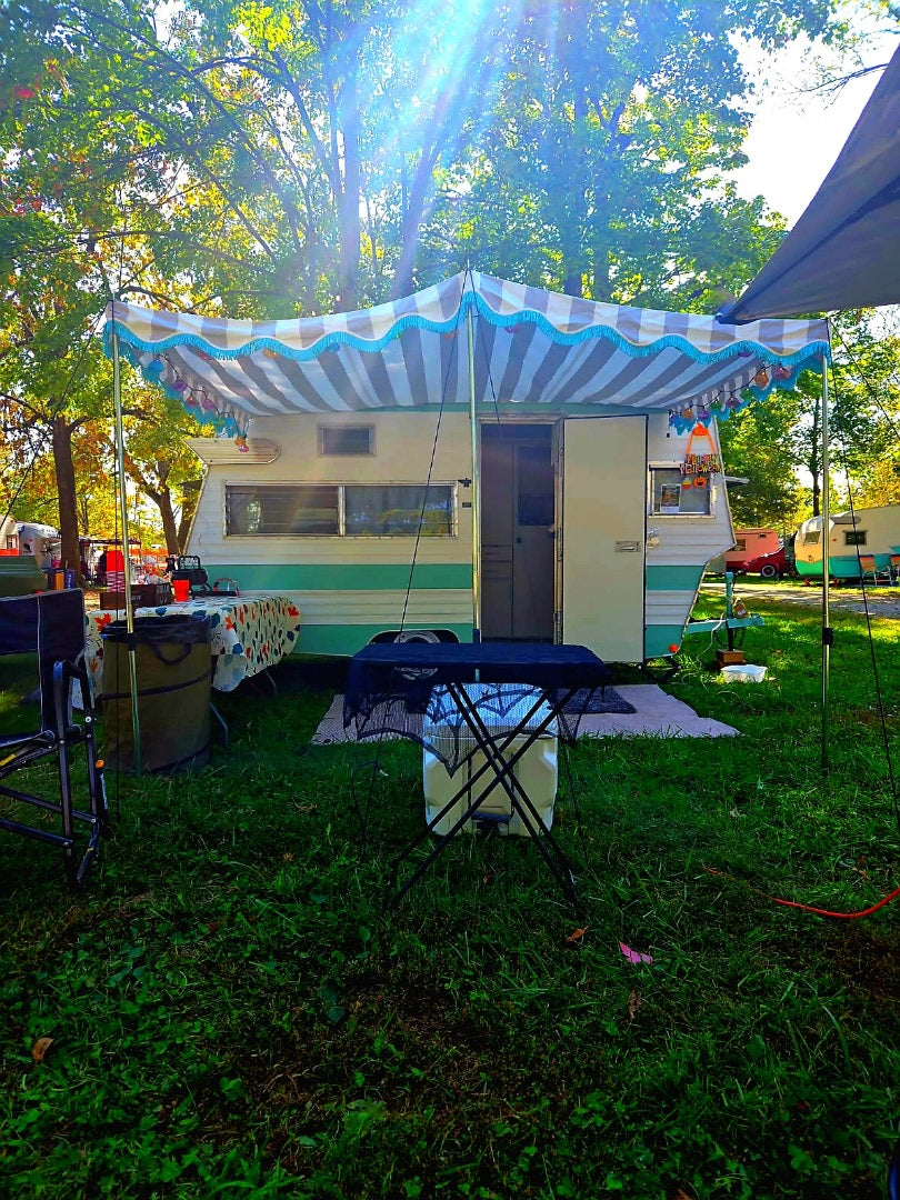 Bright sun shines on this charming vintage rv rental with a festive awning & Halloween decor at a lively campsite. — photo 9