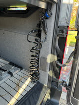 RV rental rear utility: Mounted coiled wash hose with spray nozzle & folded ladder in a camper van interior with slatted floor.