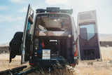 Discover this adventure-ready rv rental camper van, with its rear doors open, showing a bed, gear, and utility controls for travel.