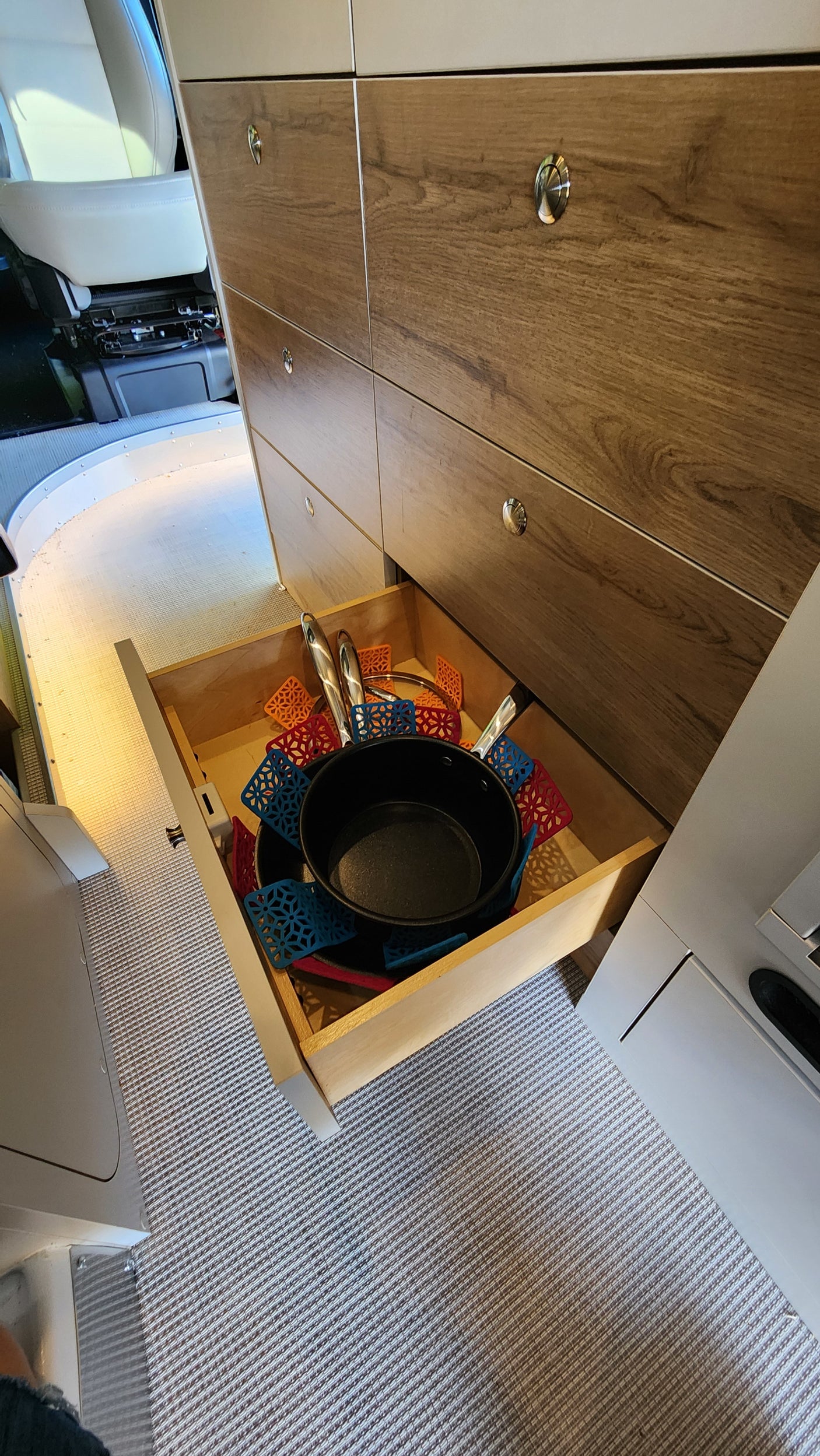 RV rental kitchen: open drawer showcasing organized pots, pans, and colorful silicone hot pads inside a modern camper.