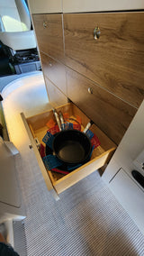 RV rental kitchen: open drawer showcasing organized pots, pans, and colorful silicone hot pads inside a modern camper.