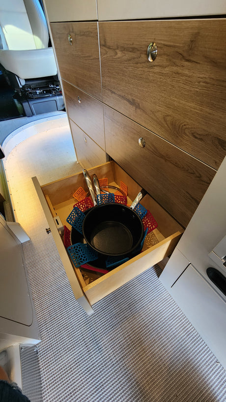 RV rental kitchen: open drawer showcasing organized pots, pans, and colorful silicone hot pads inside a modern camper.