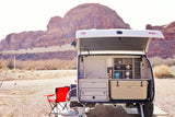White rv rental camping trailer with its rear open, revealing a full outdoor kitchen, cooler, and sink in a desert landscape.