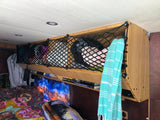 Inside an RV rental: view of a clever overhead storage net filled with essentials above a cozy bed and books.