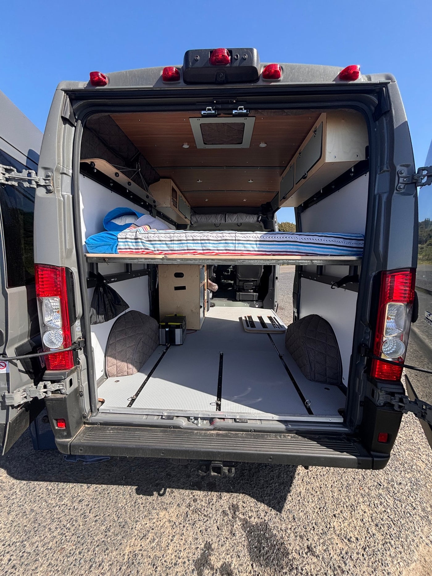 Step inside this organized camper van RV rental! Featuring a raised bed, storage, and track flooring from the open rear doors. — photo 2