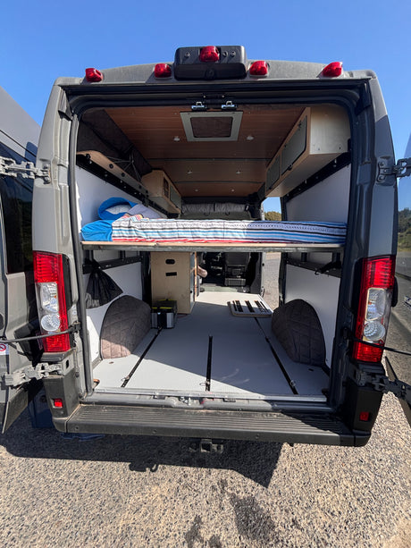 Step inside this organized camper van RV rental! Featuring a raised bed, storage, and track flooring from the open rear doors.