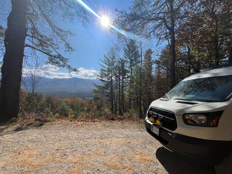 White RV rental van on a gravel road overlooking mountains & valley, perfect for scenic travel & outdoor adventure.