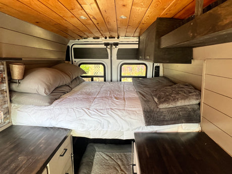 Cozy rv rental bed area inside a custom camper van, featuring a wood ceiling and ample storage for travel.