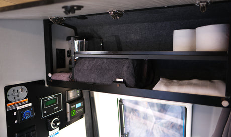 Inside an RV rental: Open cabinet with towels, toilet paper & French press. Control panel displays water heater and utility status.