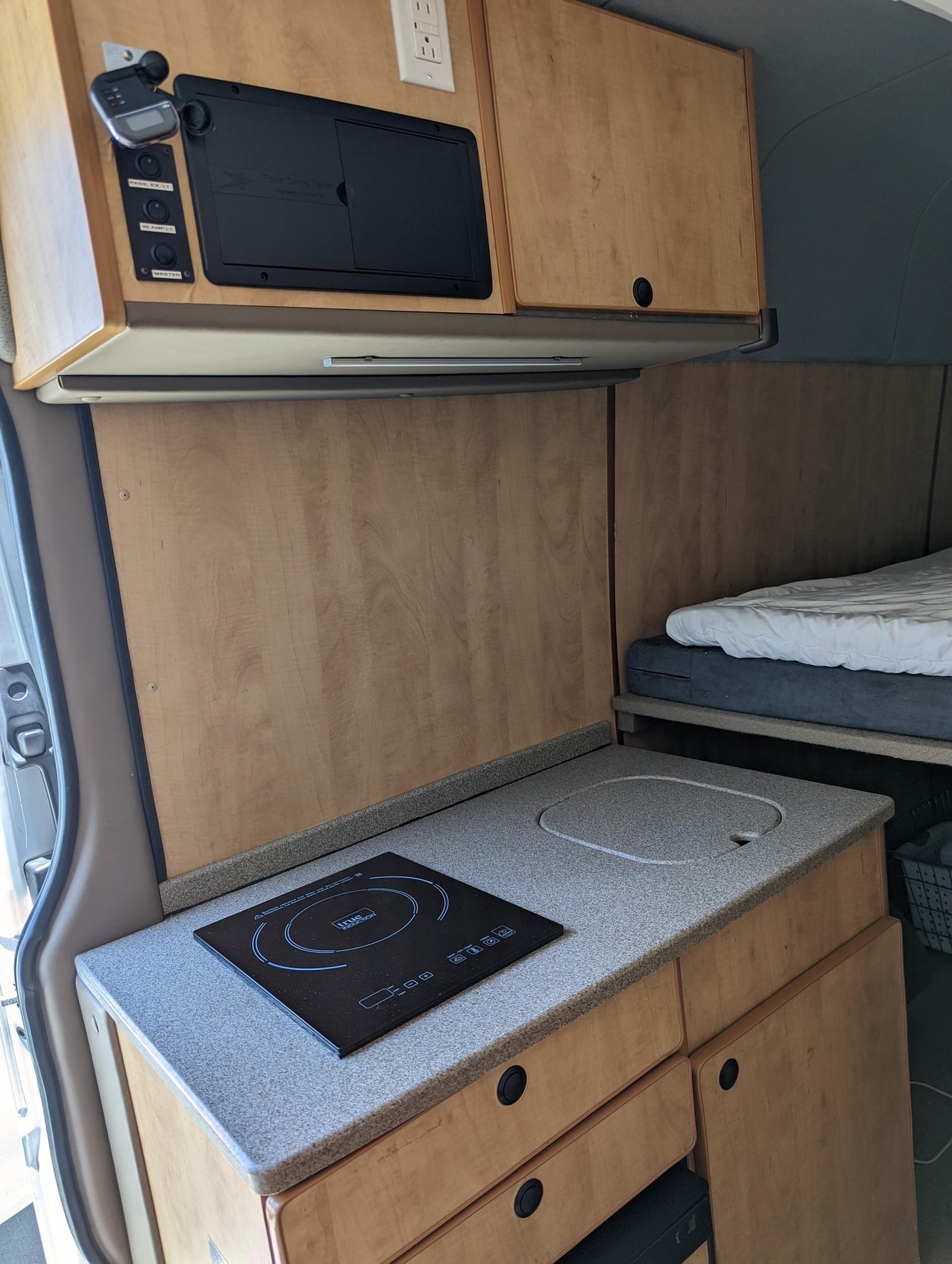 Compact RV rental interior featuring a kitchen setup with an induction cooktop, sink, wooden cabinets, and a bed. — photo 18