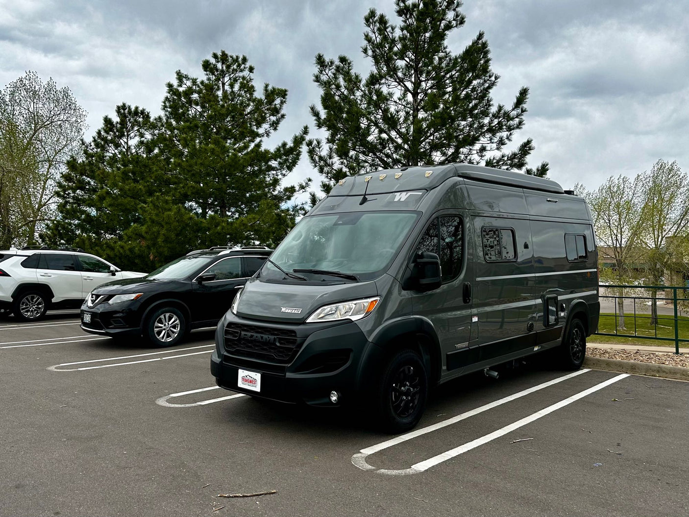 Stylish gray Winnebago camper van, ideal for rv rental, parked in a lot under a cloudy sky. Features roof lights.