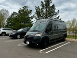 Stylish gray Winnebago camper van, ideal for rv rental, parked in a lot under a cloudy sky. Features roof lights.