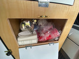 RV rental kitchen storage: Wooden cabinet holds a kettle, paper towels, and red cups. Features a brass cleat.