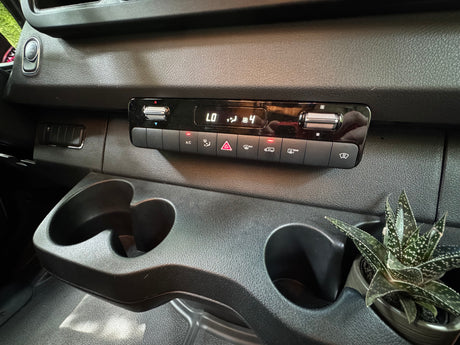 Inside an RV rental: dashboard features climate control, dual cup holders (one with a succulent), and engine start/stop button.