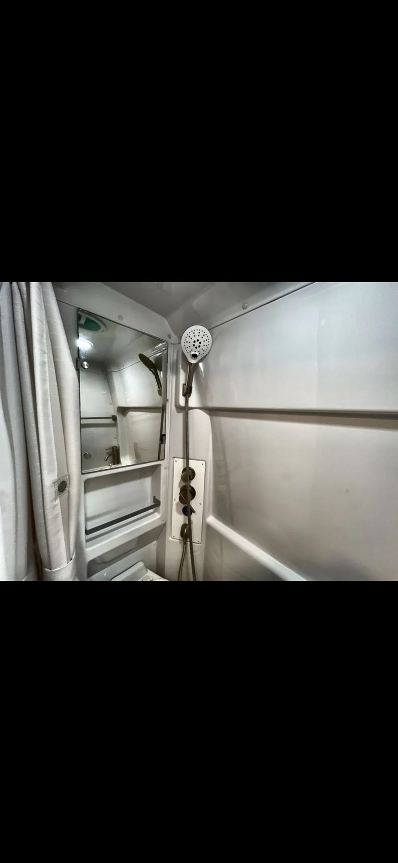 RV rental's compact bathroom features a white shower stall with handheld showerhead, controls, and a small mirror. — photo 9