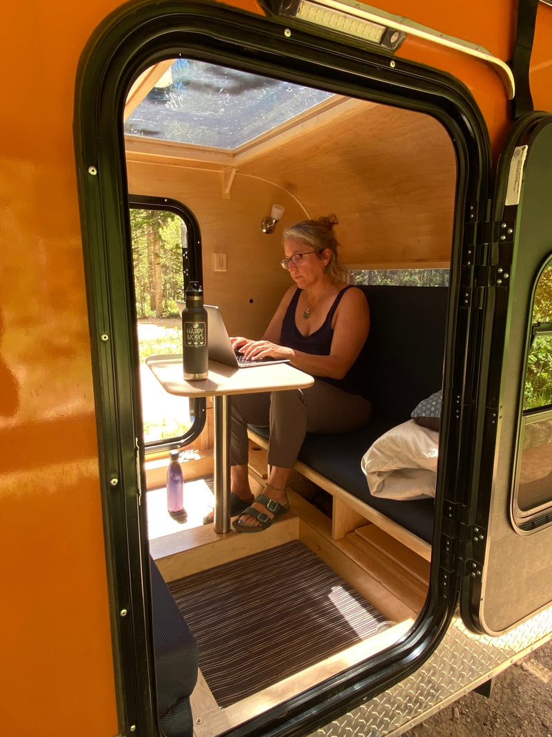 Remote work from an RV rental: A woman types on a laptop inside a small camper, with an open door view of a forest. — photo 8