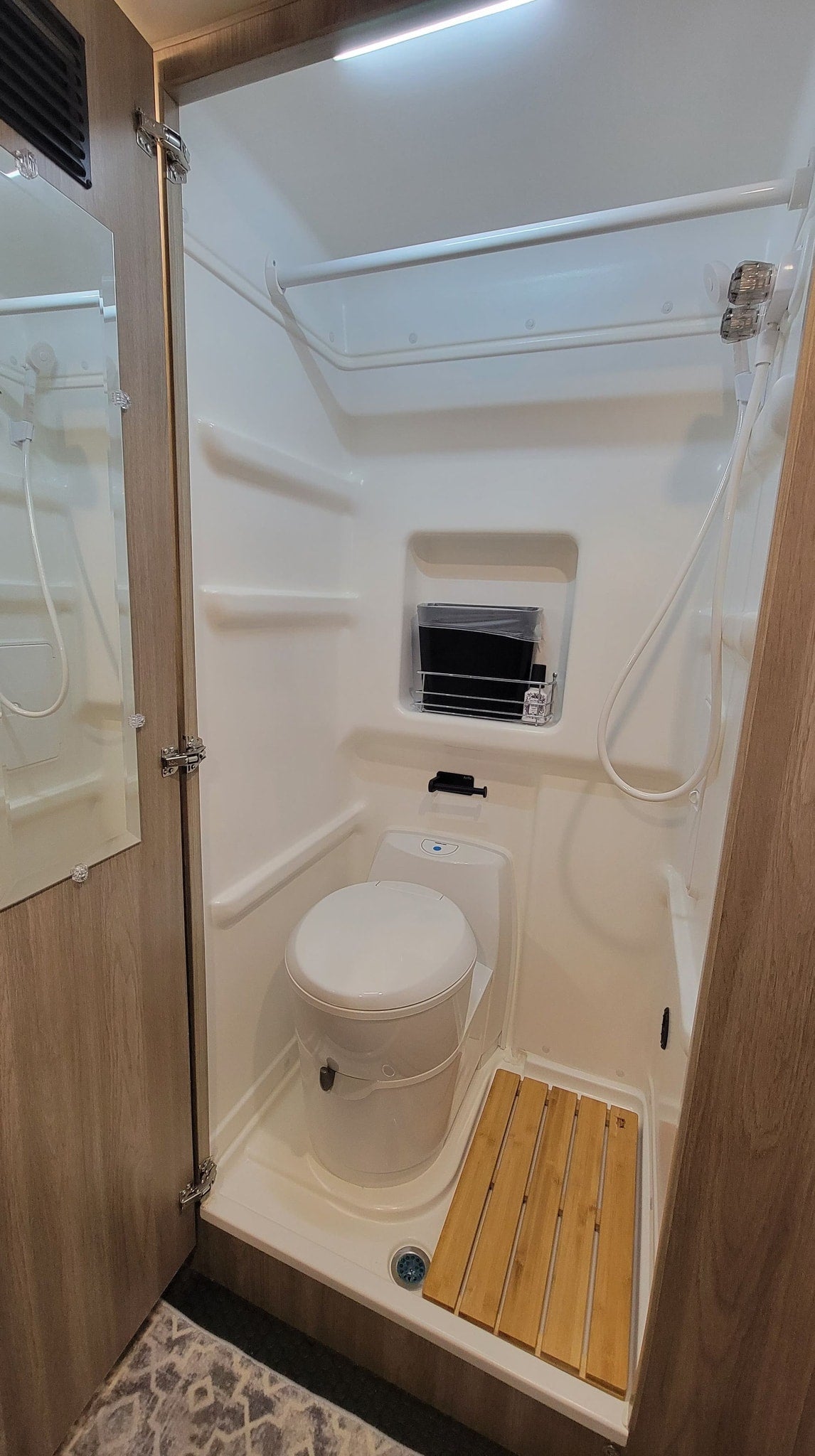 An RV rental's compact bathroom features a shower, toilet, and a practical wooden mat for efficient space utilization. — photo 11