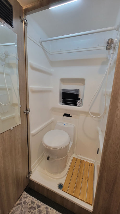 An RV rental's compact bathroom features a shower, toilet, and a practical wooden mat for efficient space utilization.