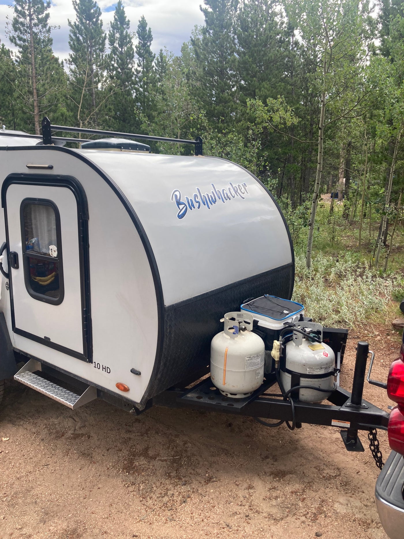 Bushwhacker 10 HD travel trailer, an RV rental, with propane tanks at a wooded campsite. — photo 2