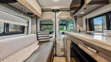 Cozy RV rental interior with kitchen, bench seating, and scenic nature views through rear windows.