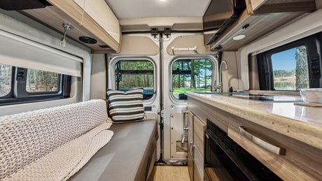 Cozy RV rental interior with kitchen, bench seating, and scenic nature views through rear windows.