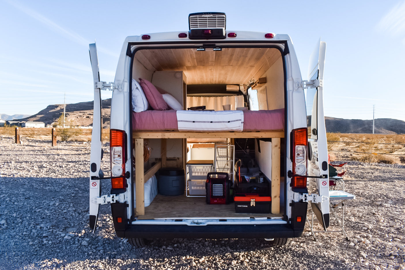 Open rear of an RV rental camper van parked in a desert landscape, revealing its cozy bed and organized storage.