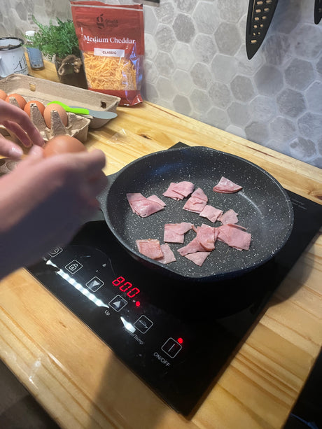 RV rental breakfast prep: Ham cooking in a pan, with eggs and cheddar ready on the compact kitchen counter.