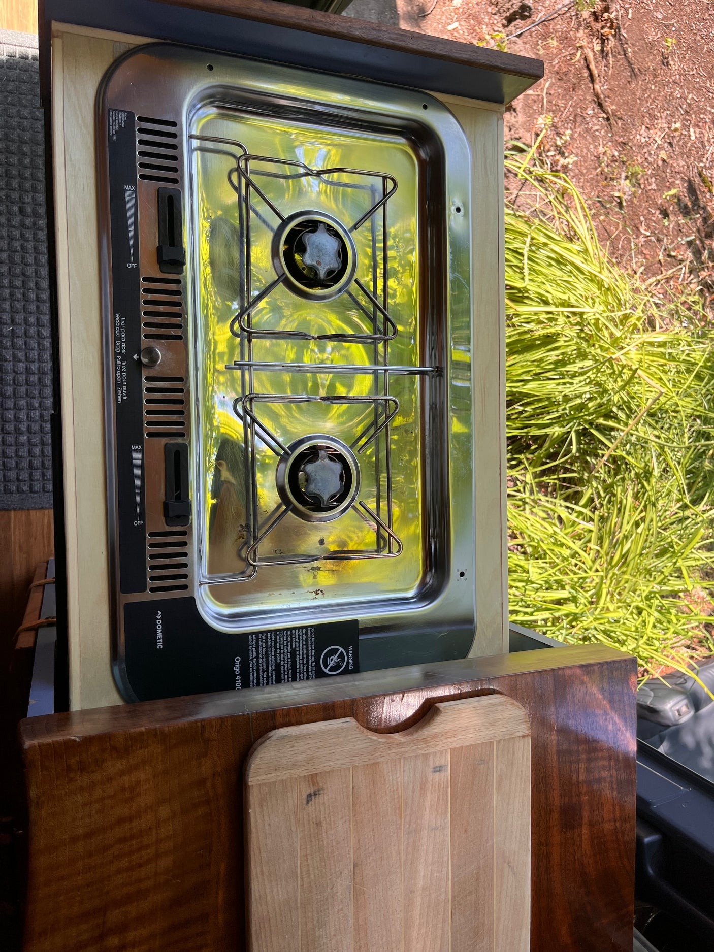 An RV rental's Dometic 2-burner stove with a wooden cutting board, ideal for cooking meals on the go in a camper.