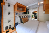 Inside a comfortable RV rental: a modern bedroom with a large bed, coastal art, and convenient controls.