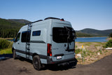 Stylish grey Mercedes Sprinter RV rental parked by a serene lake and forest, featuring a ladder and bike rack.