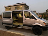 Silver pop-top Sprinter camper van, great for an rv rental. Side door open, revealing bright, cozy interior.