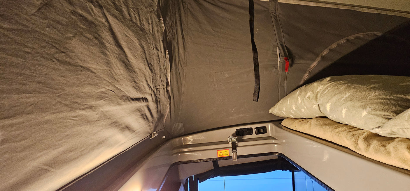 Cozy RV rental sleeping space: A pop-top camper interior with a bed, pillow, and gray fabric walls.