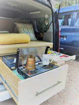 Inside a cozy RV rental: mobile kitchen with pull-out stove, kettle, 'SMILE' mug, & comfy sleeping area, perfect for camping.
