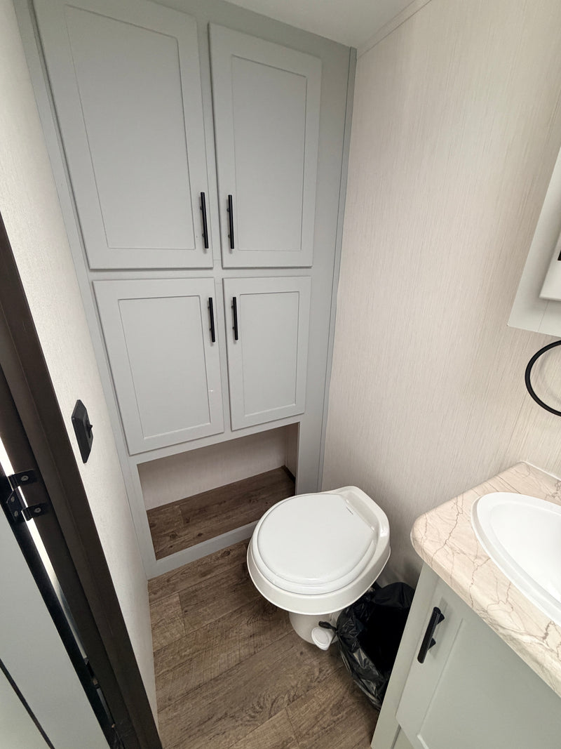 This RV rental bathroom features a compact layout with light grey cabinets, a toilet, and a sink on a marble-look counter. — photo 6