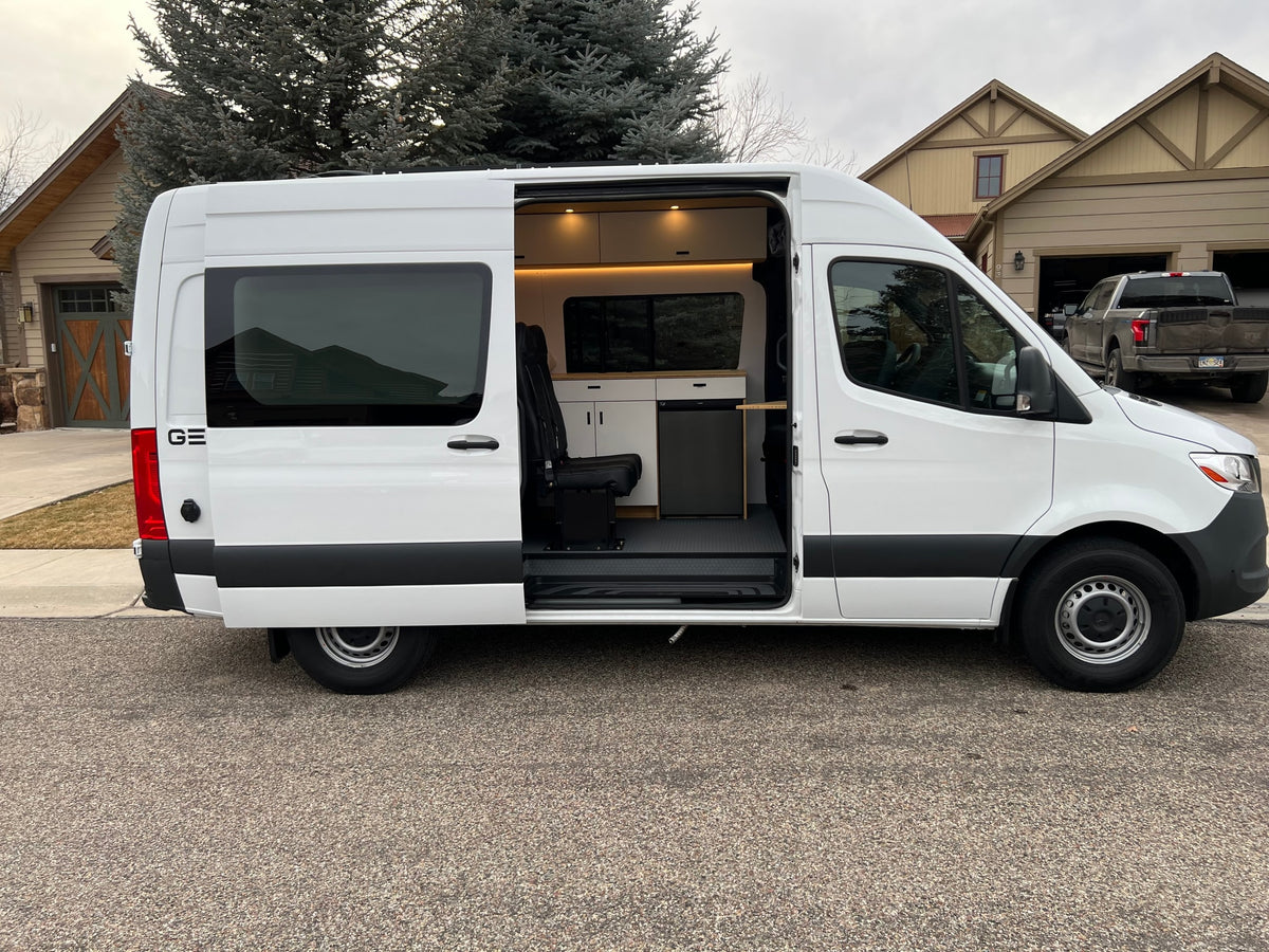 White camper van RV rental with open side door revealing custom interior including kitchenette, seating, and storage.