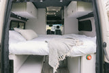 Comfortable RV rental camper van interior. Features a cozy bed, overhead storage, and windows for your road trip.