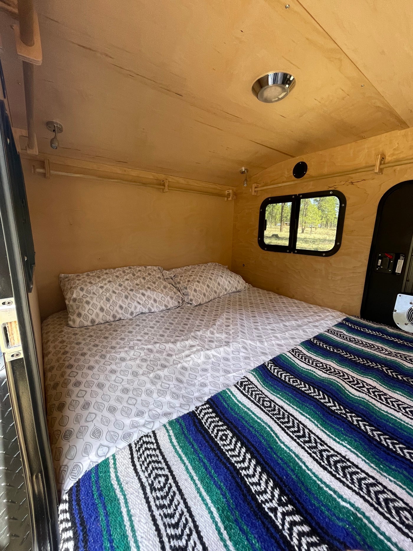 Cozy RV rental interior, featuring a comfortable bed with leaf-patterned sheets, a colorful blanket, and wood paneling. — photo 4