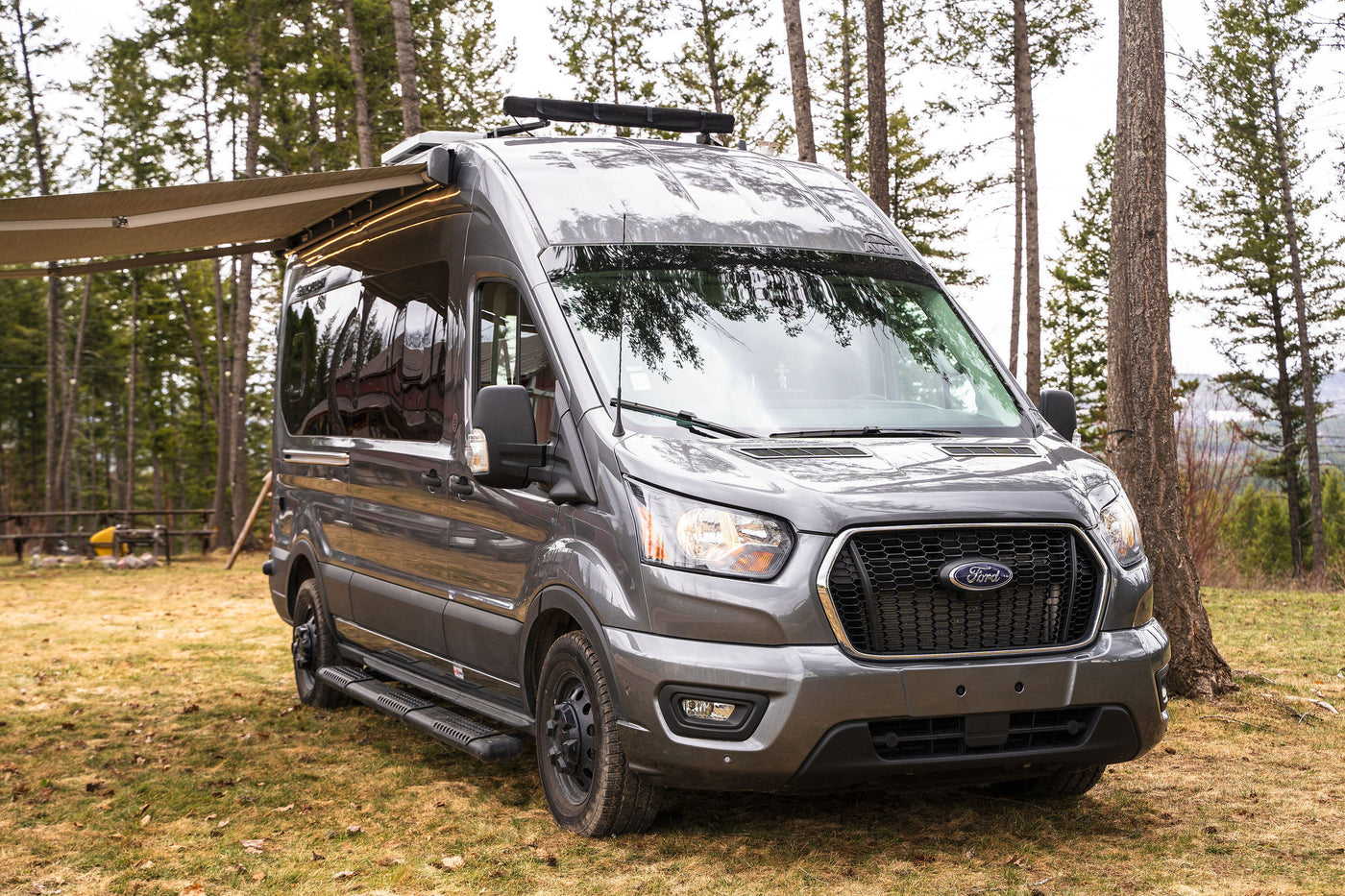  parked in a forest campsite with an extended awning & lights.|Inside a modern RV rental: compact kitchen with sink — photo 2