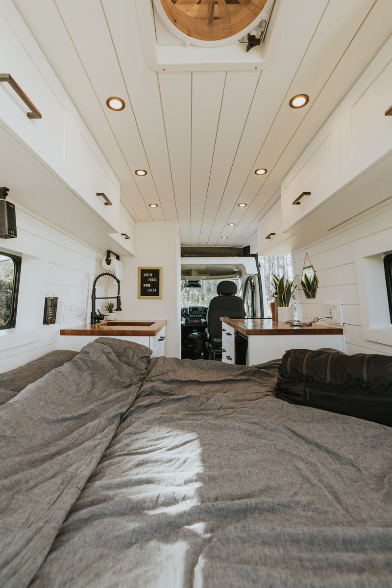 Inside a bright RV rental: features a comfy bed with grey bedding, a full kitchen area with a sink, and sleek storage solutions. — photo 5