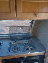 RV rental kitchen with light wood cabinets, a window, compact sink, and two-burner stovetop.