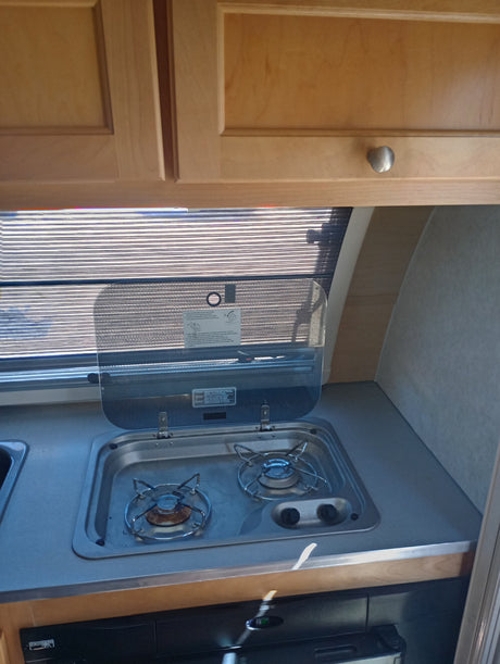RV rental kitchen with light wood cabinets, a window, compact sink, and two-burner stovetop.