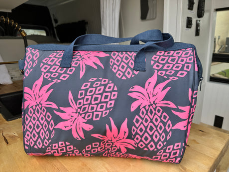 A bright pink and grey pineapple cooler bag sits in an rv rental. Perfect for van life road trips and camping adventures.