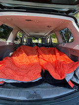 Cozy car interior transformed for camping with two orange sleeping bags. A practical and comfy alternative to an RV rental.