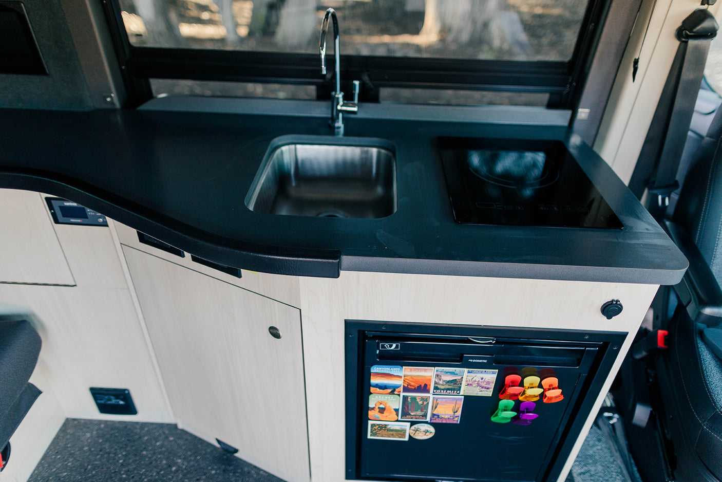 Inside an RV rental: a modern kitchen featuring a sleek black counter, sink, induction cooktop, and compact fridge.
