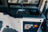 Inside an RV rental: a modern kitchen featuring a sleek black counter, sink, induction cooktop, and compact fridge.