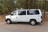 White Ford van with roof rack parked on a forest road. Explore the outdoors with this versatile rv rental.
